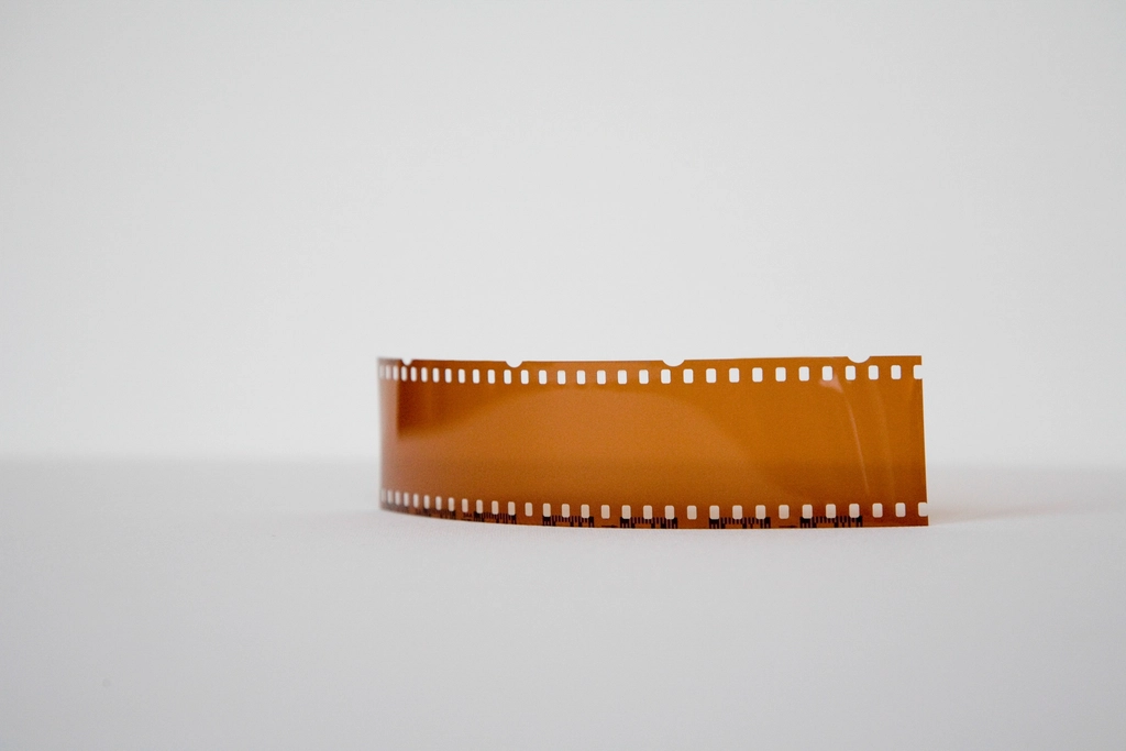 A curved strip of amber 35mm negative standing on a pale surface.